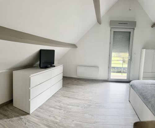 Modern attic bedroom at Le Clos de la Vallée cottage with white dresser, TV, bed, and glass door overlooking garden in