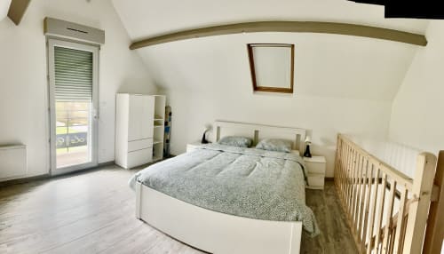Bright attic bedroom at Le Clos De La Vallée cottage with white bed, wooden crib, storage, glass balcony door overlooking