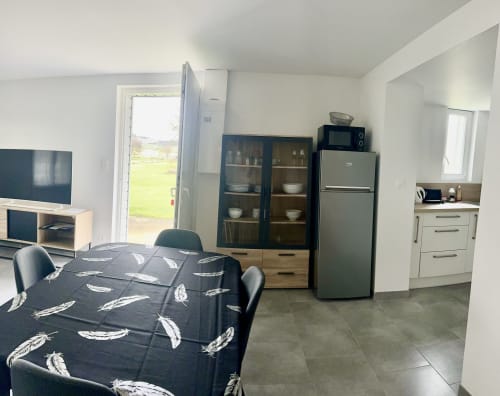 Open-plan cottage kitchen and living area with dining table, refrigerator, black cabinets, and garden view at Le Clos De La