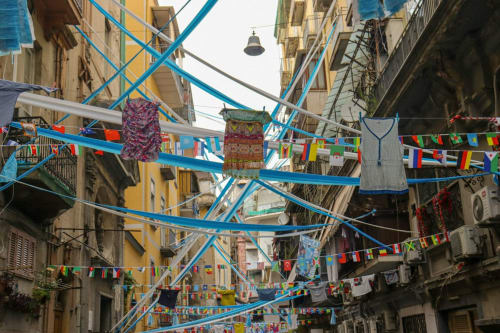 Via colorata di Napoli con stendibiancheria blu, bandiere internazionali e bucato tra edifici storici