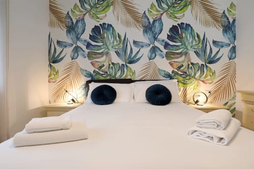 Camera da letto dell'hotel Re di Roma con carta da parati tropicale, biancheria bianca, cuscini blu navy e comodini moderni a Roma