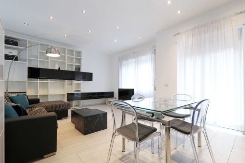 Moderno appartamento a Roma con soggiorno open-plan, zona pranzo, tavolo in vetro, scaffali neri e vista sulla città