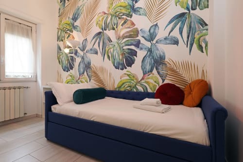 Letto navy con biancheria color crema nell'appartamento Re di Roma a Roma, sfondo con carta da parati botanica