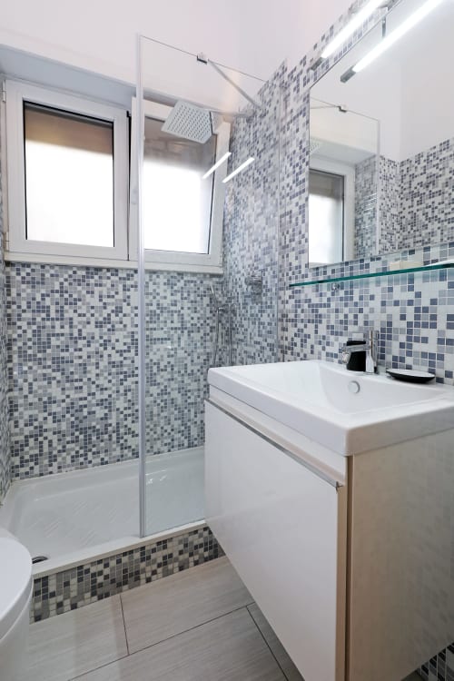 Bagno moderno dell'hotel Re di Roma a Roma con piastrelle mosaico blu, doccia walk-in, lavabo bianco e vista sulla città