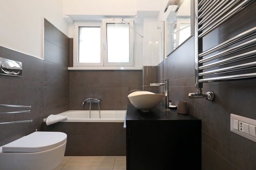 Bagno moderno dell'hotel Re di Roma a Roma con piastrelle scure, lavabo a bacinella e vasca con vista sulla città
