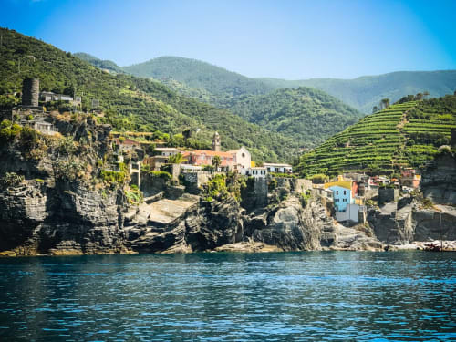 Vernazza village with colorful houses perched on cliffs overlooking turquoise Mediterranean waters and terraced vineyards.