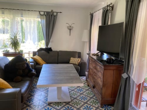 Modern living room with dark sofa, flat-screen TV, wooden dresser, and patterned blue tiles at Domaine des Lavarines,