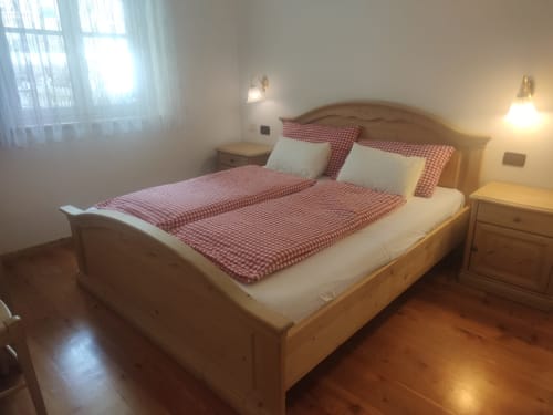 Bright bedroom at Residence Rodolon in Mazzin with wooden bed, red checkered bedding, nightstands, and mountain views