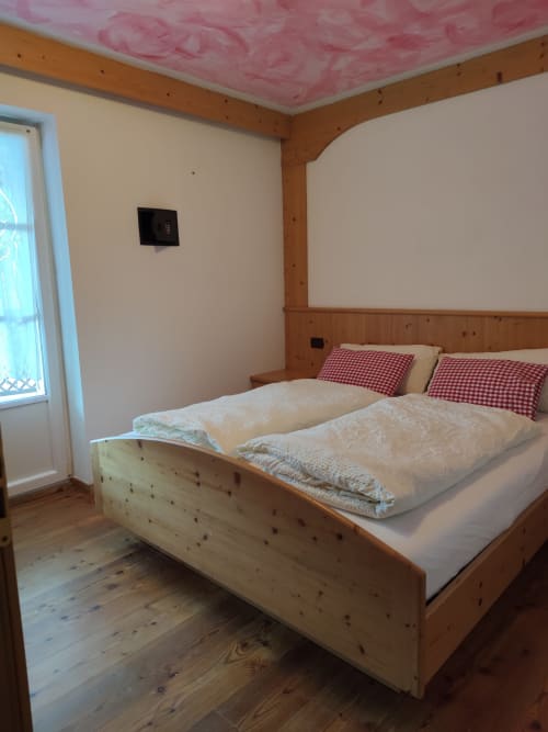 Cozy wooden bedroom in Dona Apartment at Residence Rodolon, Mazzin, with queen bed, red checkered pillows, and garden views
