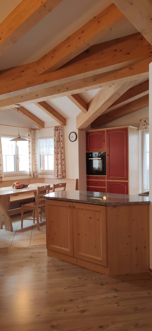 Sassolungo Apartment kitchen with wooden beams, red cabinetry, and island at Residence Rodolon, Mazzin