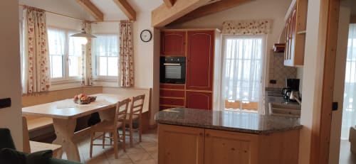 Küche und Essbereich des Sassolungo-Apartments in der Residenz Rodolon in Mazzin mit Holzbalken und roten Schränken