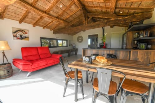 Séjour et salle à manger moderne aux Gites De La Grande Borderie avec canapé rouge, poutres apparentes, table à manger et cuisine ouverte