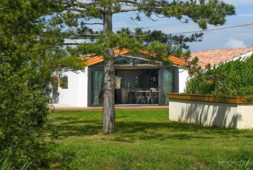 Villa moderne aux Gîtes De La Grande Borderie avec portes vitrées, terrasse et pelouse soignée bordée de pins