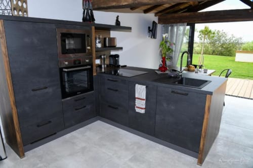 Cuisine moderne noire avec accents bois, appareils inox et vue sur le jardin à la villa Gites De La Grande Borderie