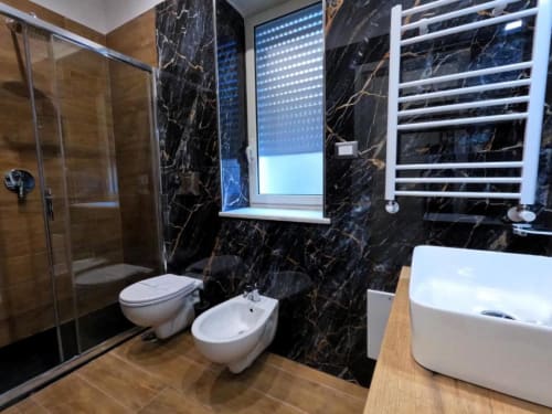 Bagno moderno presso Blackwoody Contemporary a Napoli con pareti in marmo nero, sanitari bianchi e box doccia