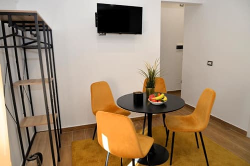 Moderna zona pranzo di Blackwoody BCH TRIBUNALI a Napoli con sedie arancioni, tavolo tondo nero e TV a schermo piatto