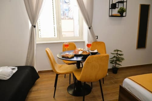 Zona pranzo nella suite BCH TRIBUNALI dell'hotel Blackwoody Napoli con sedie gialle senape, tavolo nero e finestre con vista sulla città