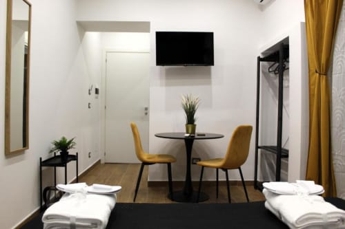 Moderna camera d'hotel presso Blackwoody Contemporary Hospitality a Napoli con due letti, tavolo da pranzo, TV a parete e tende dorate