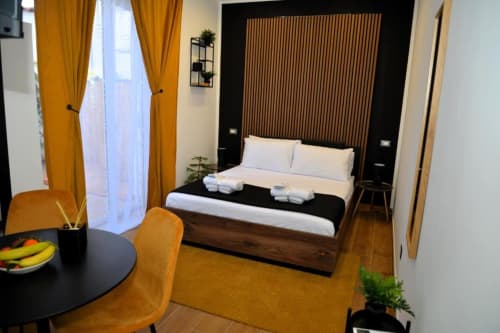 Camera matrimoniale moderna al Blackwoody Contemporary Hospitality di Napoli con letto in legno, tende dorate e vista sul giardino