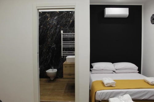 Camera Blackwoody BCH TRIBUNALI a Napoli con letto, cuscini bianchi, plaid giallo e bagno privato con parete in marmo nero.