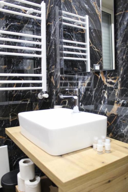 Bagno moderno con lavabo bianco su mobile in legno, pareti in marmo nero con venature dorate e scaldasalviette