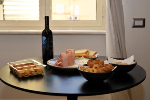 Tavola di vini e salumi con prosciutto, pasticcini e pane in camera d'hotel a Napoli con vista dalla finestra