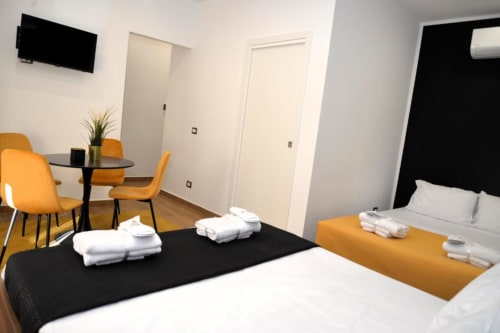 Camera Quadrupla Superior al Blackwoody Contemporary Hospitality di Napoli con due letti, sedie arancioni, tavolo da pranzo e