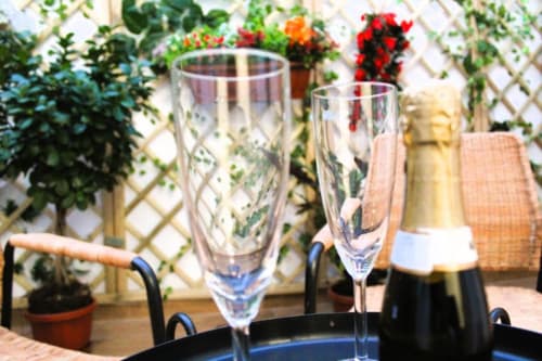 Flute di champagne e bottiglia sulla terrazza della Sala Tribunali di Blackwoody BCH a Napoli, con vista sul giardino fiorito