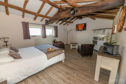 Chambre spacieuse aux Gîtes de la Grande Borderie avec poutres en bois apparent, lit blanc, mobilier en cuir marron et bois