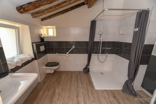 Salle de bains accessible aux Gîtes de la Grande Borderie à Saint-Gervais avec douche à l'italienne, toilettes et poutres en bois
