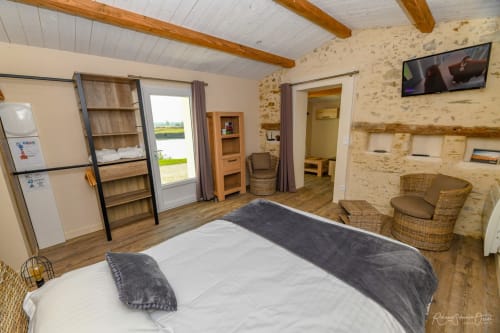 Chambre spacieuse à Gites De La Grande Borderie avec lit queen-size, murs en pierre, poutres en bois, coin salon et TV