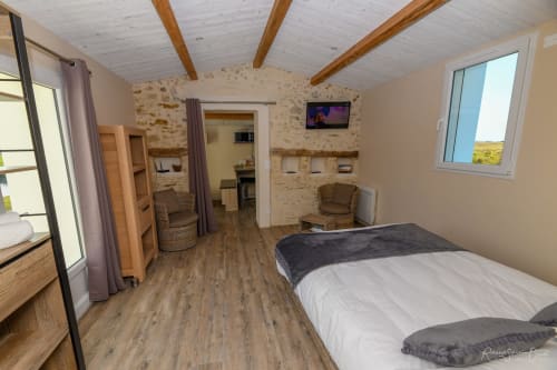 Spacieuse chambre de villa aux Gites De La Grande Borderie, Saint Gervais avec poutres en bois, murs en pierre, TV et coin salon