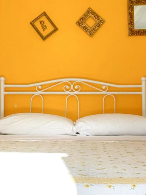 Camera da letto giallo brillante con letto in ferro battuto bianco e cuscini presso SoleMagia B&B a Vernazzo, Italia