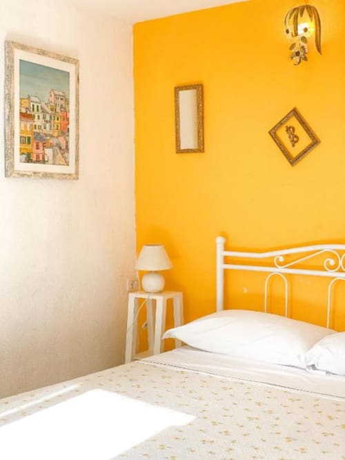 Camera luminosa giallo sole presso SoleMagia B&B a Vernazzo con letto in ferro bianco e arte paesaggistica italiana colorata