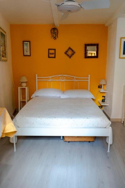 Camera da letto arancione luminosa presso SoleMagia B&B a Vernazzo con letto in metallo bianco e dettagli gialli