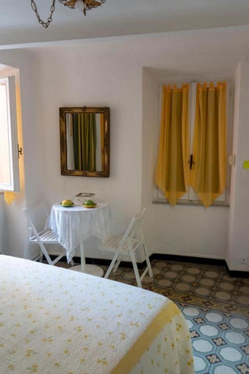 Luminosa camera a SoleMagia Vernazzo con tende gialle, tavolino da pranzo e pavimento con piastrelle decorate