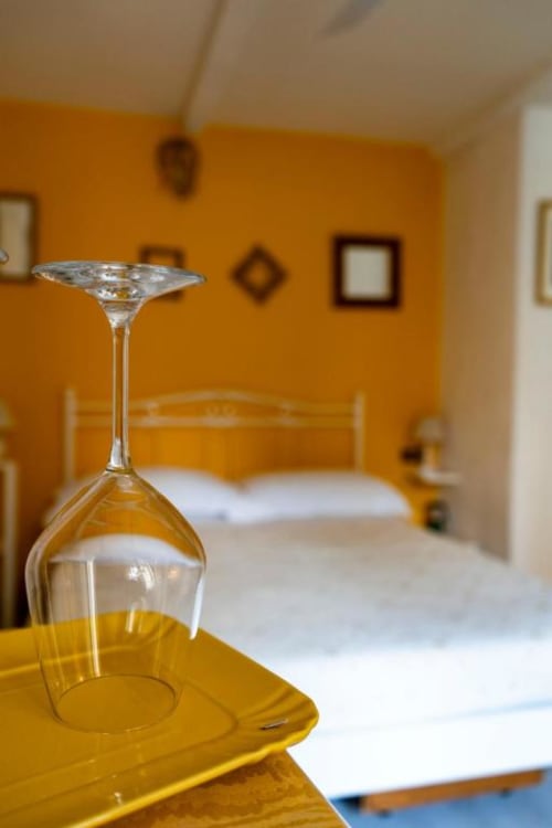 Calice di vino su tavolo giallo nella camera SoleMagia con vista sulla camera di Vernazzo dalle pareti arancioni
