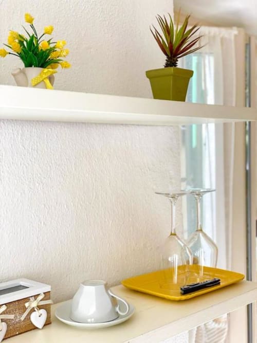 Composizione in vetrina nella stanza SoleMagia con fiori gialli, pianta in vaso, calici di vino e arredi con vista su Vernazza
