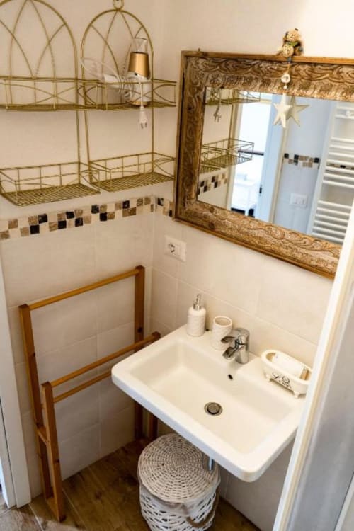 Bagno della SoleMagia a Vernazzo con lavabo bianco, specchio dorato, pareti piastrellate e scaffali organizzati