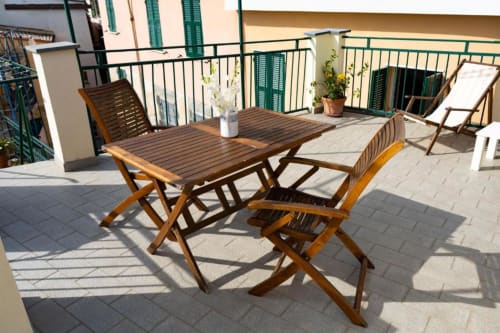 Terrazza in legno con tavolo da pranzo e sedie presso il B&B SoleMagia a Vernazzo, Italia, con vista sulla città e persiane verdi