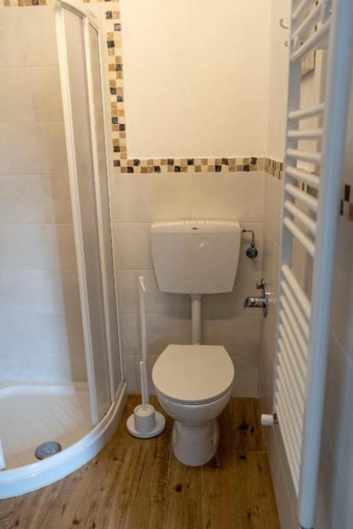 Bagno compatto e luminoso nella camera B&B SoleMagia con toilette bianca, cabina doccia e bordatura decorativa in maiolica a Vernazzo