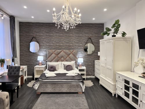 Luxury studio apartment bedroom at Railway Hotel with dark wood accent wall, crystal chandelier, white furniture, and modern