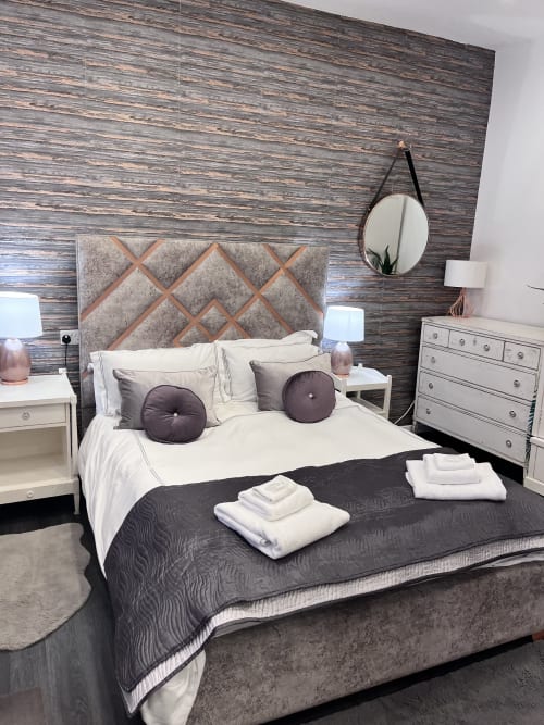 Luxury studio apartment bedroom at The Railway Hotel with wood-textured wall, upholstered headboard, white bedding, and