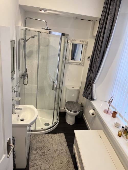 Modern bathroom with curved glass shower enclosure, white sink, toilet, and dark flooring at The Railway Hotel Haydon Bridge