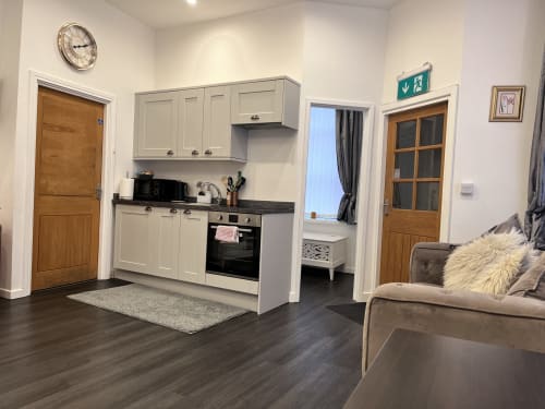 Modern studio apartment kitchenette with cream cabinets, black stovetop, and seating area at The Railway Hotel, Haydon Bridge