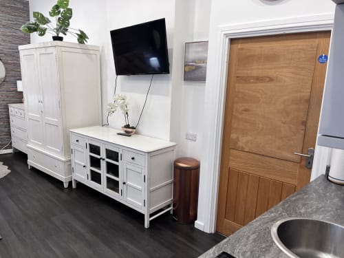 Modern kitchenette and living area in Haydon Bridge luxury studio apartment with white cabinetry, TV, and wooden door