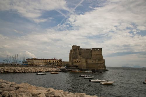 La fortezza Castel dell'Ovo che domina il porto di Napoli con barche ormeggiate e storici edifici sul lungomare