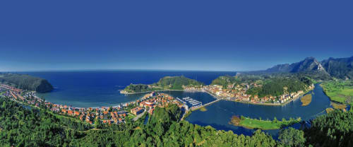 Aerial view of Ribadesella coastal town surrounded by green forests, mountains, and blue waters in Asturias, Spain
