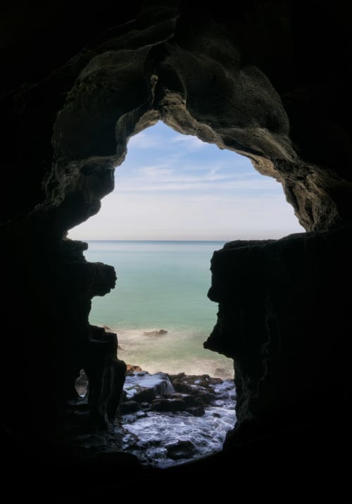 Grotta marina rocciosa che si affaccia su acque turchesi e spiaggia vicino a Bari, Italia