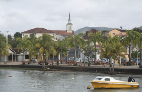 Bateau jaune et blanc amarré au port de Trois-Îlets avec église coloniale, palmiers et vue sur l'hôtel Kay Betty